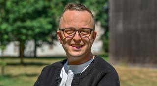 Een man een bril die een zwarte vest aanheeft in een groene omgeving